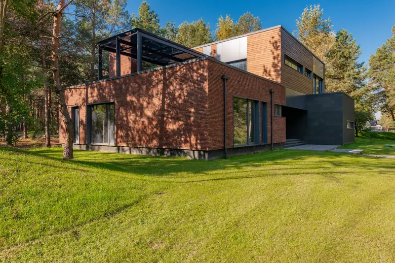 Full garden view of a low-rise house with brick walls, timber upper storey and a black roof terrace frame.