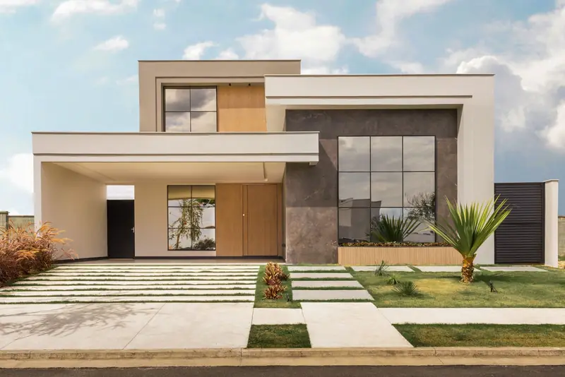 Contemporary two-storey house photographed straight on, with cream walls, dark stone, tall glazing and a planted front garden.