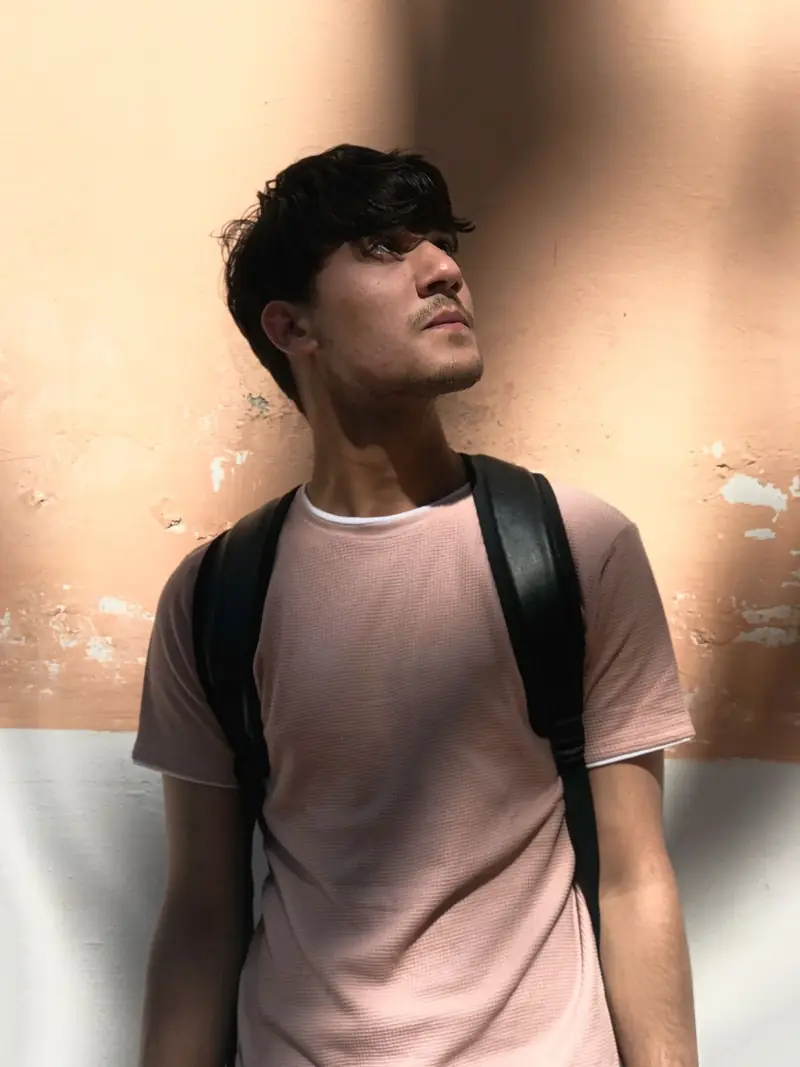 Portrait of a man in a neutral shirt against a textured wall.