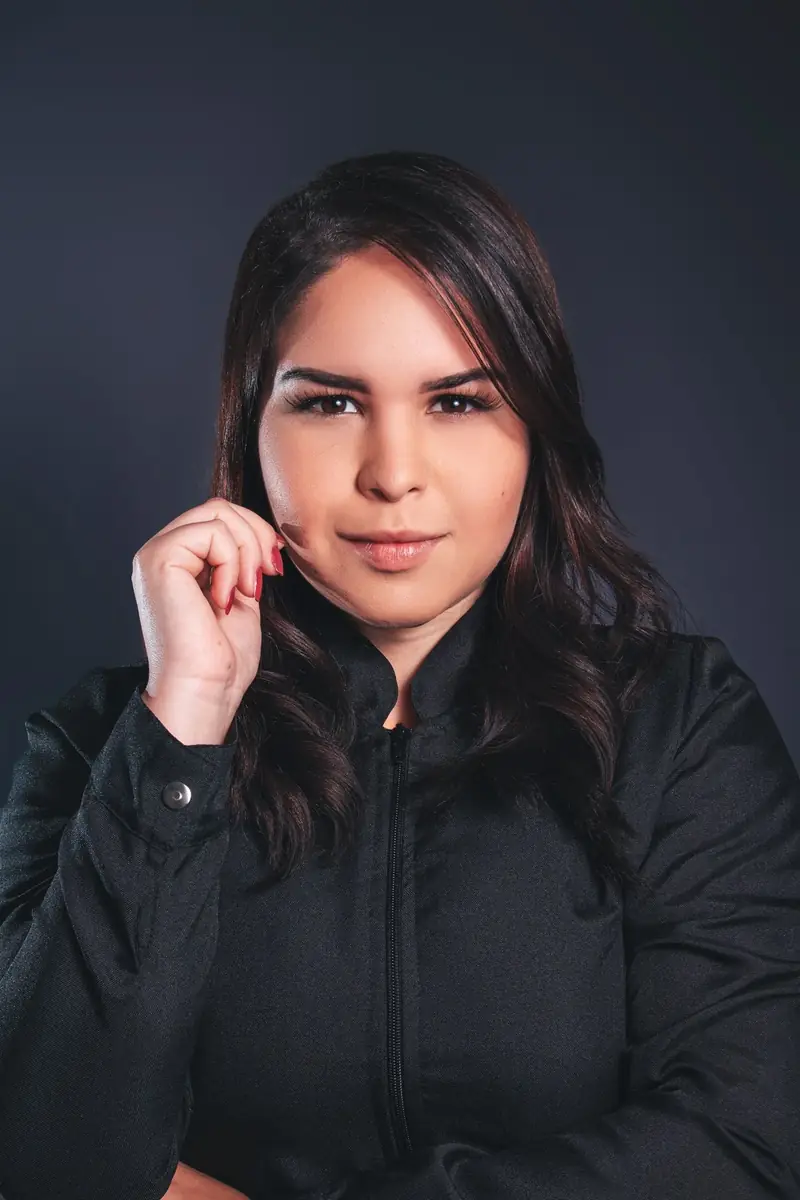 Portrait of a woman in a black shirt against a dark studio backdrop.