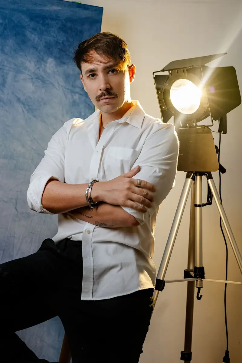 Portrait of a man wearing a white shirt, standing in a softly lit studio.