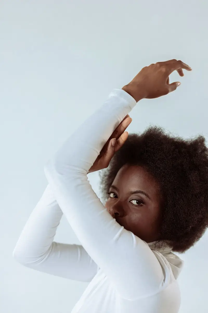 Portrait of a woman wearing a white blouse, with one arm raised.